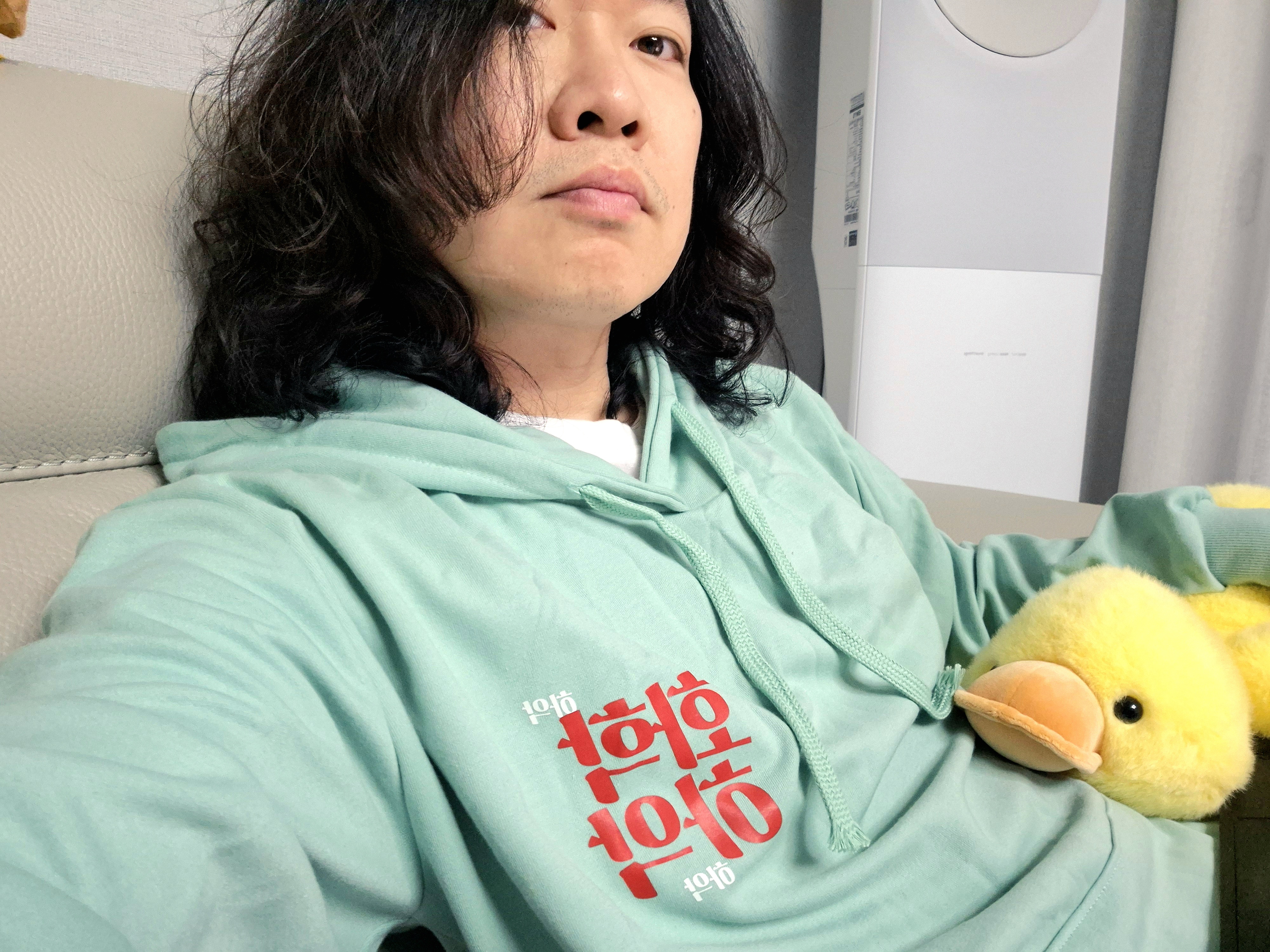 민트색 화학하악 후드티를 입고 노란 오리 인형을 안은 모습